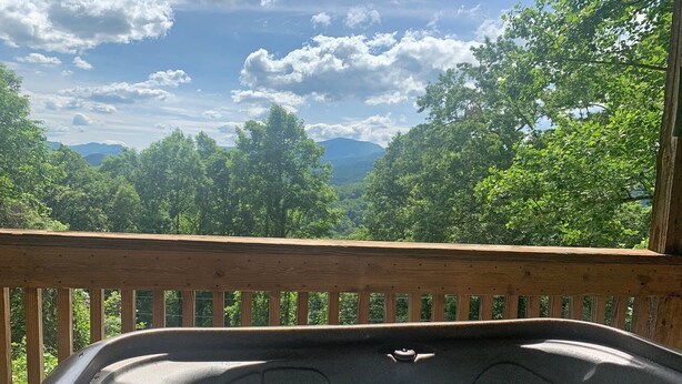 A hot tub on a wooden deck with a view of trees and mountains. - True Log Cabin (Bryson City)
