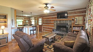 A cozy cabin interior with a fireplace, wooden furniture, and a kitchen area. - True Log Cabin (Bryson City)