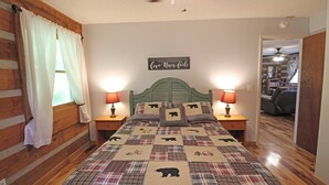 A cozy bedroom with a wooden headboard, a quilted bedspread with animal prints, two bedside lamps, and a motivational quote on the wall. - True Log Cabin (Bryson City)