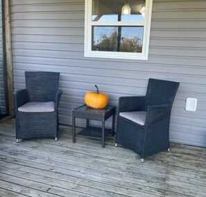 Een veranda met twee rieten stoelen, een klein tafeltje en een pompoen.