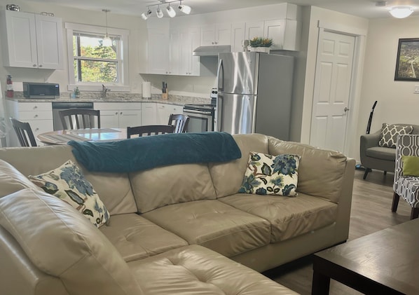 A modern kitchen with white cabinets, a stainless steel refrigerator, and a dining area with a table and chairs.