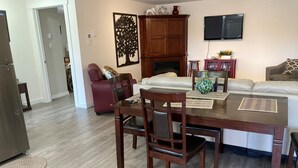 Ein Wohnzimmer mit Esstisch, Stühlen, einer Couch, einem Kamin und einem Fernseher.
