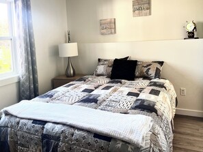 Een opgemaakt bed met een geborduurd quilt, een bedlampje en een muur met twee decoratieve objecten.