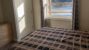 Ein Schlafzimmer mit einem Bett, einer Kommode und einem Fenster mit Blick auf eine verschneite Landschaft.