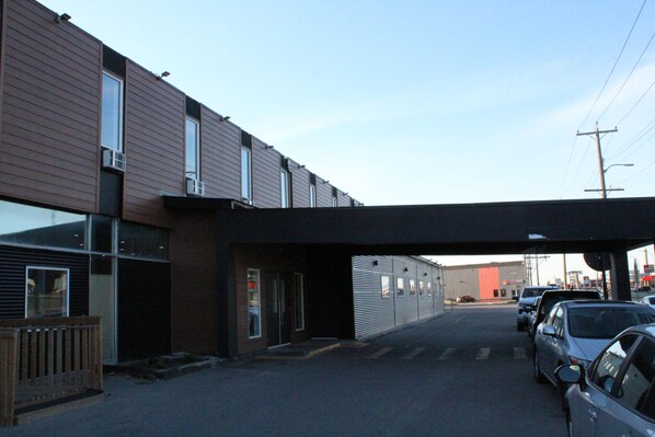 A building with a covered walkway, parked cars, and a clear sky. - Grand Royal Legacy (Winnipeg)