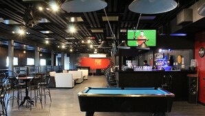 Zona de bar con mesa de billar, taburetes y una televisión mostrando un evento deportivo.