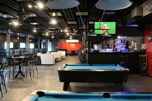 Zona de bar con mesa de billar, taburetes y una televisión mostrando un evento deportivo.