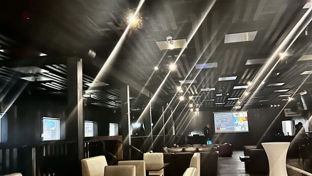 Un interior moderno con zonas de estar, mesas y una pantalla grande mostrando contenido.