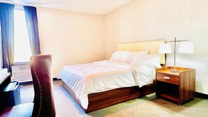 Una habitación de hotel con cama, escritorio, silla y mesita de noche con lámparas.