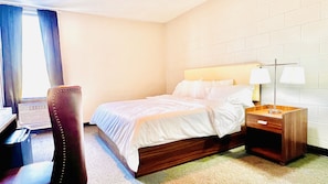 Una habitación de hotel con cama, escritorio, silla y mesita de noche con lámparas.