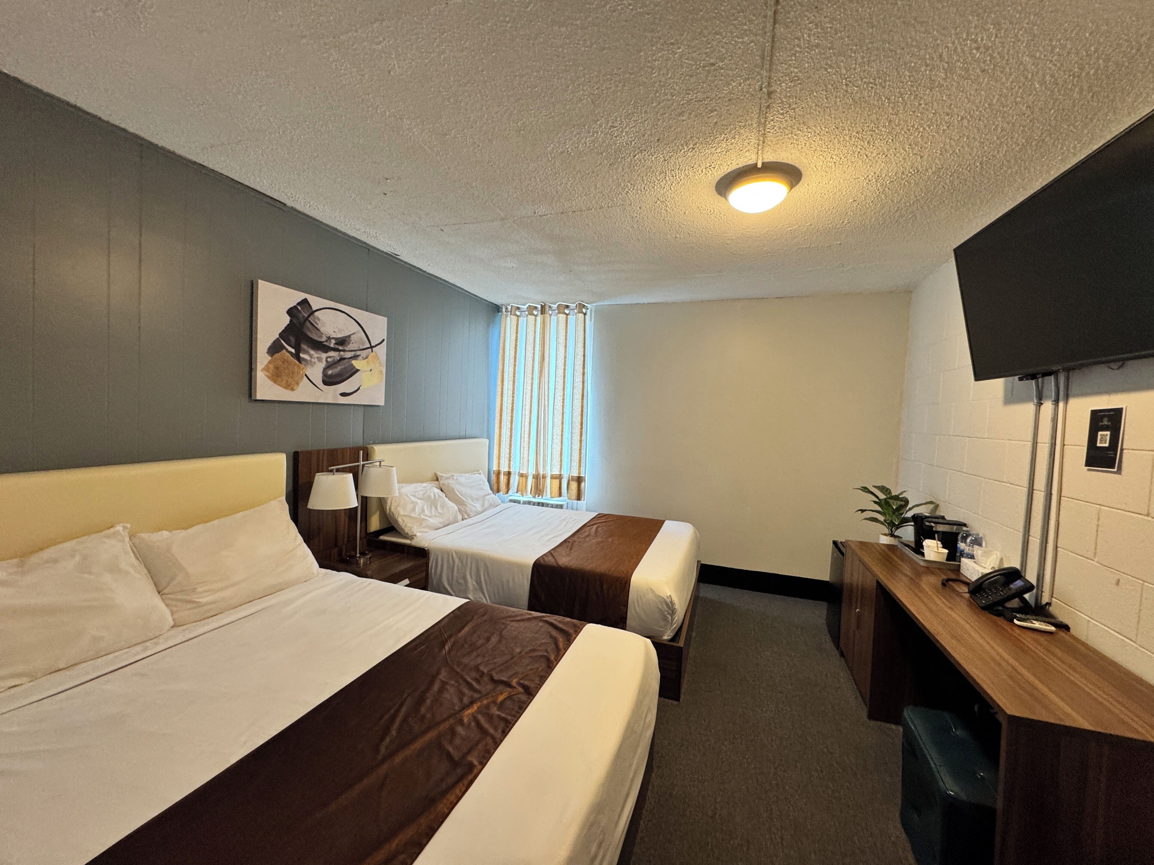 Una habitación de hotel con dos camas, un escritorio, un televisor y un ventanal con cortinas.