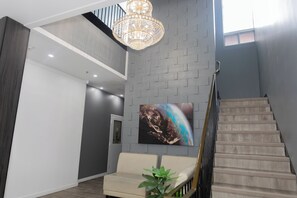 A modern interior with a staircase, a chandelier, a sofa, and a wall-mounted artwork. - Grand Royal Legacy (Winnipeg)