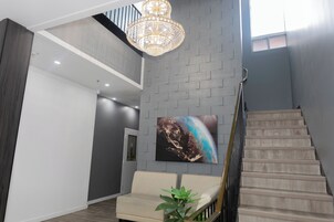 Un interior moderno con una escalera, una araña, un sofá y una obra de arte en la pared.