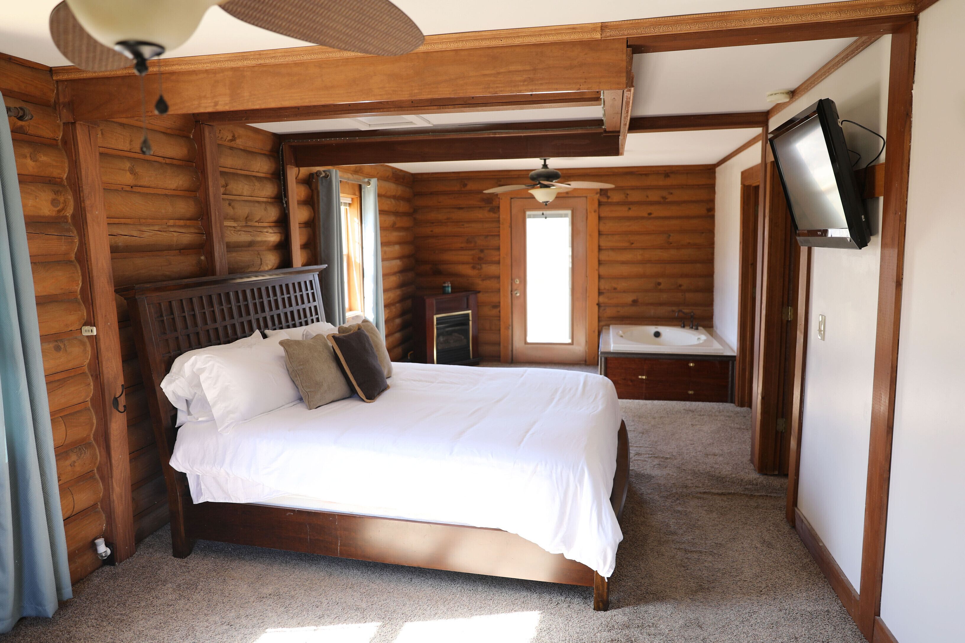Une chambre à coucher de style chalet, avec un lit en bois, un ventilateur de plafond et un téléviseur fixé au mur.