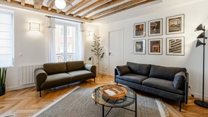 A living room with two sofas, a coffee table, and a floor lamp. There are framed pictures on the wall and a window with curtains. - Appartement Grenelle - Welkeys (Paris)