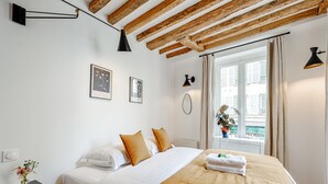 A bedroom with a bed, a nightstand, a window with a view, and wooden beams on the ceiling. - Appartement Grenelle - Welkeys (Paris)