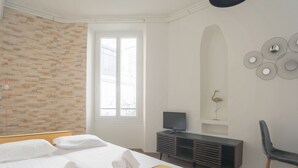 Un dormitorio con cama, escritorio, silla, televisor y una pared con detalles decorativos.