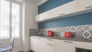 Una cocina moderna con armarios blancos, una pared de acento azul, un salpicadero con diseño y un tostador rojo.