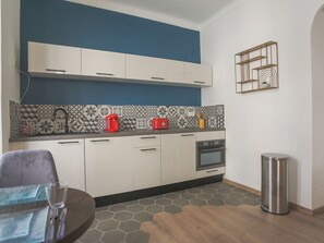 Une cuisine moderne avec des armoires blanches, un mur d’accent bleu, un dosseret à motifs et une poubelle en acier inoxydable.