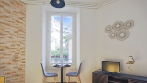 A modern living room with a stone wall, a dining area with two chairs, a TV on a stand, and a decorative wall piece. - Studio Nid Doré - Welkeys (Cannes)