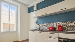 A kitchen with white cabinets, a black countertop, and a red coffee maker. - Studio Nid Doré - Welkeys (Cannes)