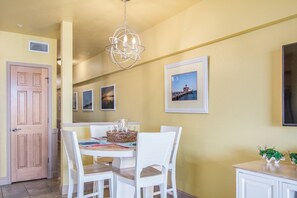 A dining area with a round table, white chairs, a chandelier, and framed pictures on the wall.