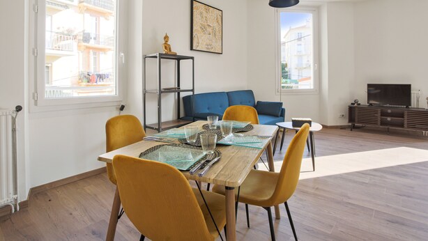 Ein modernes Wohnzimmer mit Esstisch, gelben Stühlen, einem blauen Sofa und einem Fernsehmöbel.