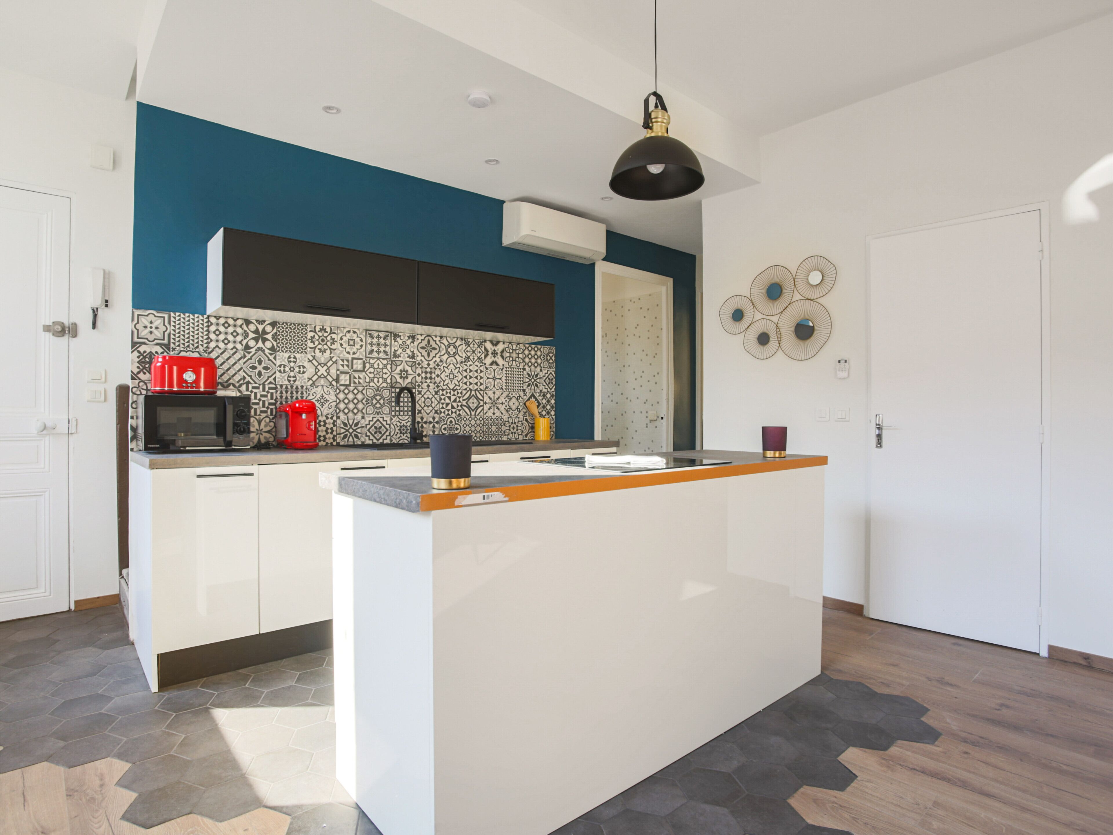 Een moderne keuken met een centraal kookeiland, een magnetron, een rode koffiezetapparaat en een hanglamp.