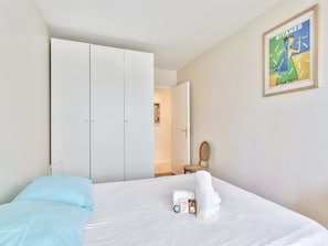 Quarto de hotel com cama, guarda-roupa, cadeira e quadro na parede.