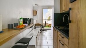 A modern kitchen with a wooden countertop, a sink, and a dining area with a chair and table. - Studio Doris - Welkeys (Montpellier)