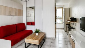 A modern living space with a red sofa, a wooden coffee table, and a kitchen area with a TV and a coffee machine. - Studio Doris - Welkeys (Montpellier)