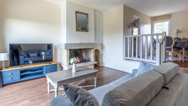 A living room with a fireplace, a sofa, a TV, and a dining area with chairs and a table. - Appartement Amirauté - Welkeys (Tourgéville)