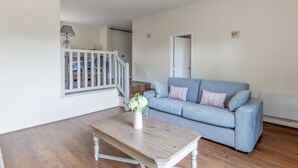 A spacious living room with a wooden coffee table, a blue sofa, and a staircase leading to an upper floor. - Appartement Amirauté - Welkeys (Tourgéville)