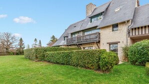 A two-story stone house with a balcony, a well-maintained lawn, and a hedge. - Appartement Amirauté - Welkeys (Tourgéville)