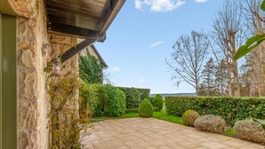 A paved patio with stone tiles, surrounded by well-maintained hedges and trees. - Appartement Amirauté - Welkeys (Tourgéville)