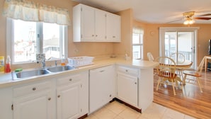 A kitchen with white cabinets, a dishwasher, and a dining area with wooden chairs and a table. - Beachfront Old Orchard Beach Condo w/ Balcony (Old Orchard Beach)