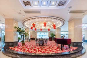 Un vestíbulo de hotel con una zona de estar circular, un televisor de pantalla plana grande y un suelo alfombrado en color rojo.