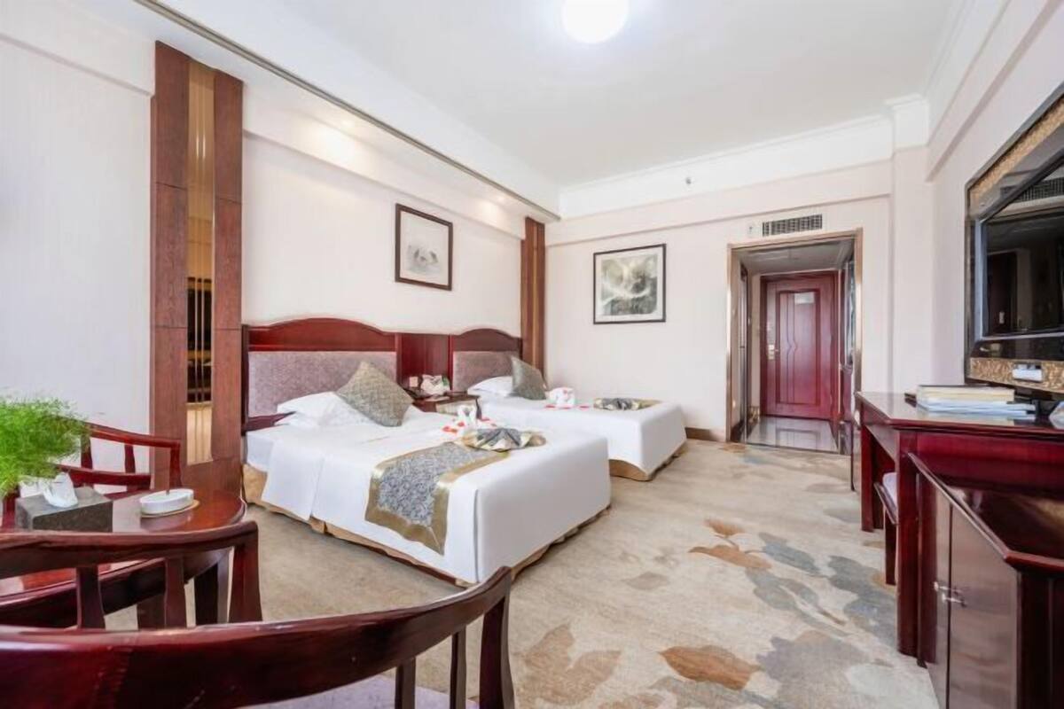 A hotel room with two beds, a desk, a chair, a TV, and a door.