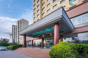 Un hotel de varios pisos con un acceso cubierto, zona de estacionamiento y cielo despejado.