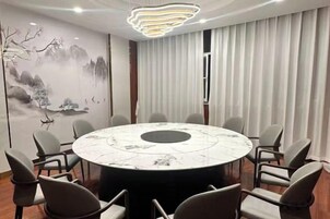 A conference room with a round table surrounded by chairs, a mural on the wall, and a large window with curtains.
