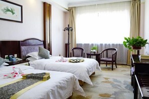 A hotel room with two beds, a desk, a chair, a potted plant, and a window with curtains. - Hongrui Holiday Hotel (Linxia)