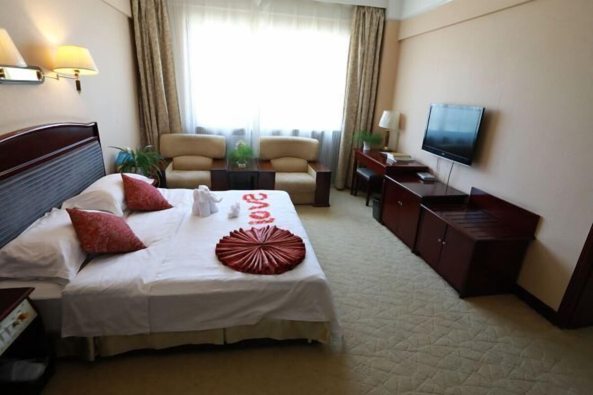 A hotel room with a bed, two chairs, a TV, and a desk.