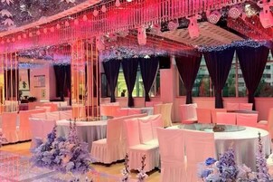 Un salón de banquetes con mesas redondas, sillas blancas y un techo decorado con adornos colgantes.