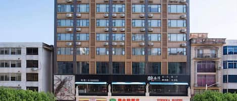 A multi-story hotel with a prominent sign at the top, several ground-level shops, and a well-maintained entrance area.