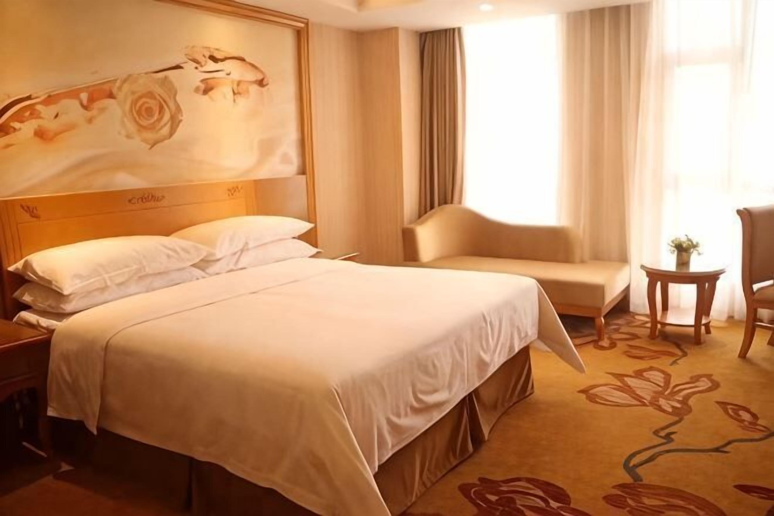 Ein Hotelzimmer mit Bett, einem Sessel, einem kleinen Tisch und einem Bild an der Wand.