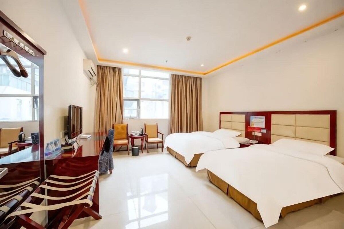 A hotel room with a large bed, a desk, a chair, a TV, and a window with curtains.