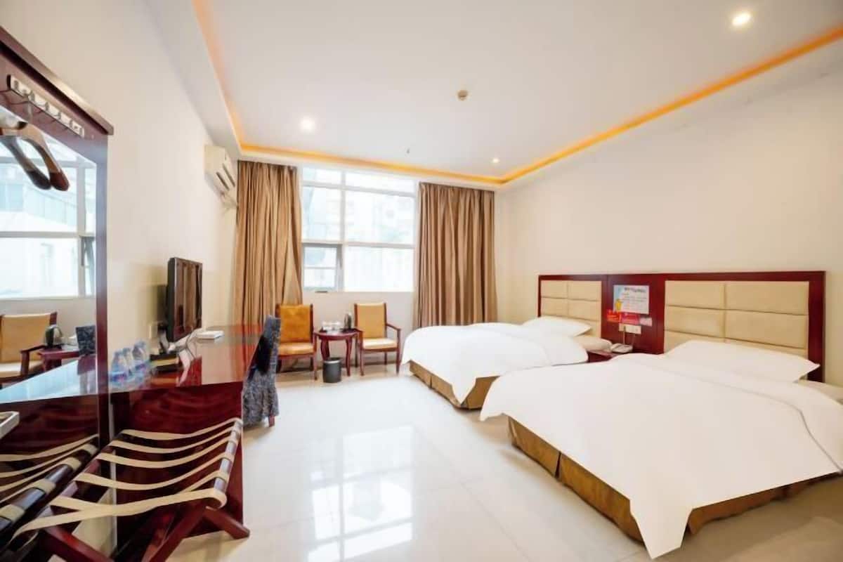 A hotel room with two beds, a desk with a chair, a TV, and a window with curtains.