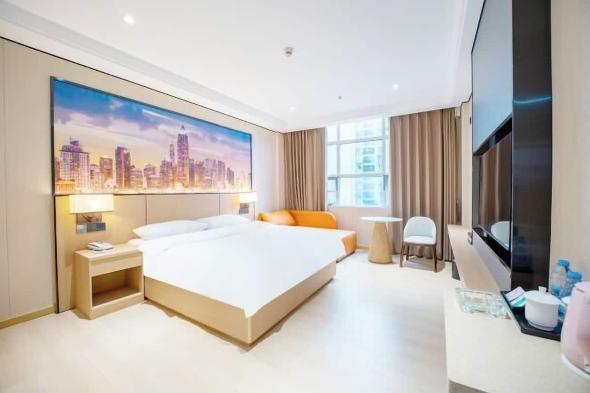 A modern hotel room with a large bed, a cityscape painting, a TV, and a desk with a chair.