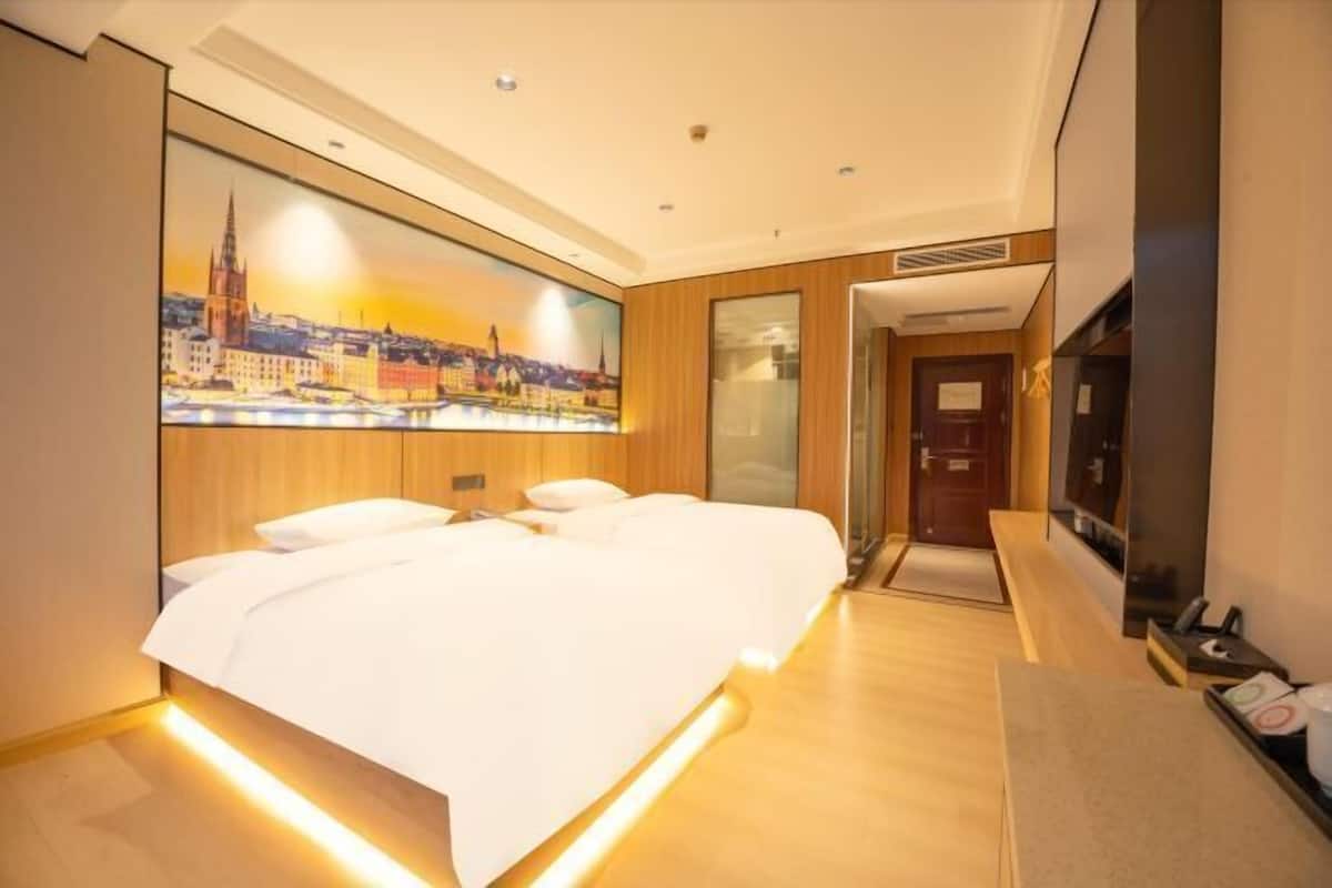 A hotel room with a bed, a painting of a cityscape, a television, and a wooden floor.