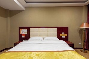 A hotel room with a bed, a nightstand, a lamp, and a wall-mounted sign. - Huifeng Hotel (Shaoguan)